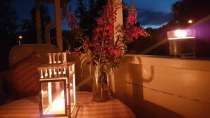 A table with a glass candle holder and a glass candle, a vase with flowers, and a grill in the background.