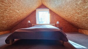 A small, cozy attic bedroom with a sloped ceiling, a single bed, two bedside lamps, and a window providing natural light.