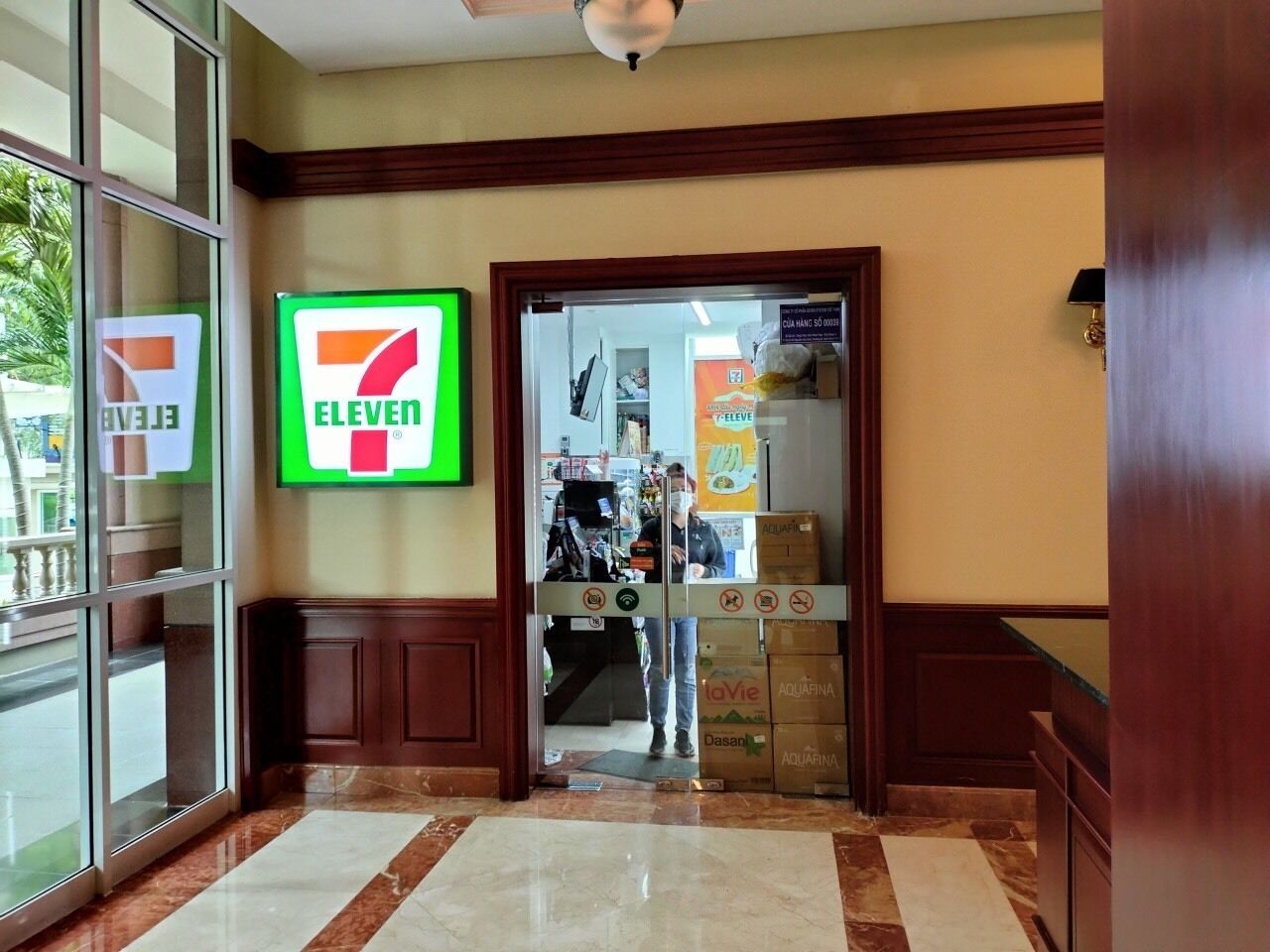 A 7-Eleven convenience store entrance with a glass door, a tiled floor, and a wooden interior.