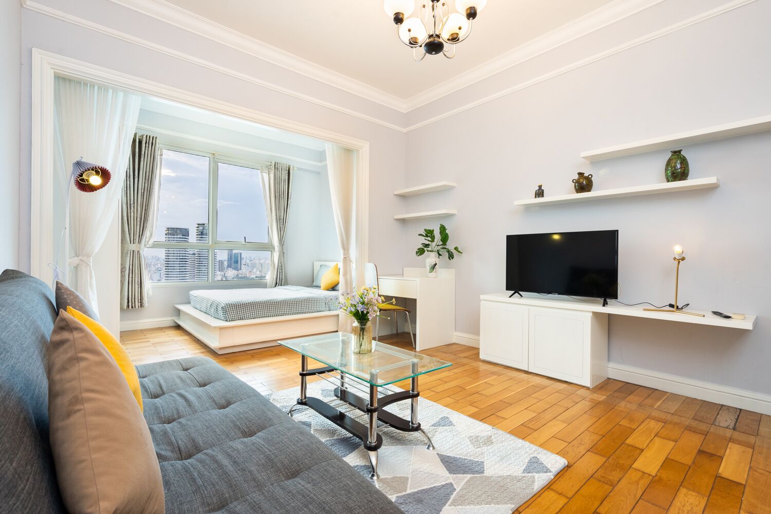 Ein modernes Wohnzimmer mit einer Couch, einem Glastisch, einem Fernseher und Blick auf die Stadt durch große Fenster.