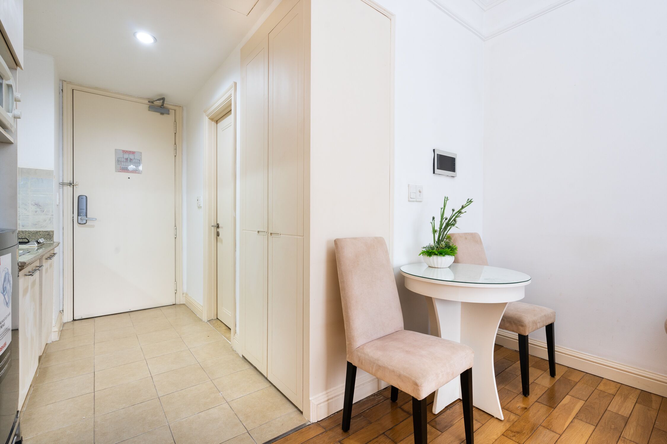 A room with a dining table, two chairs, a potted plant, and a white wall.