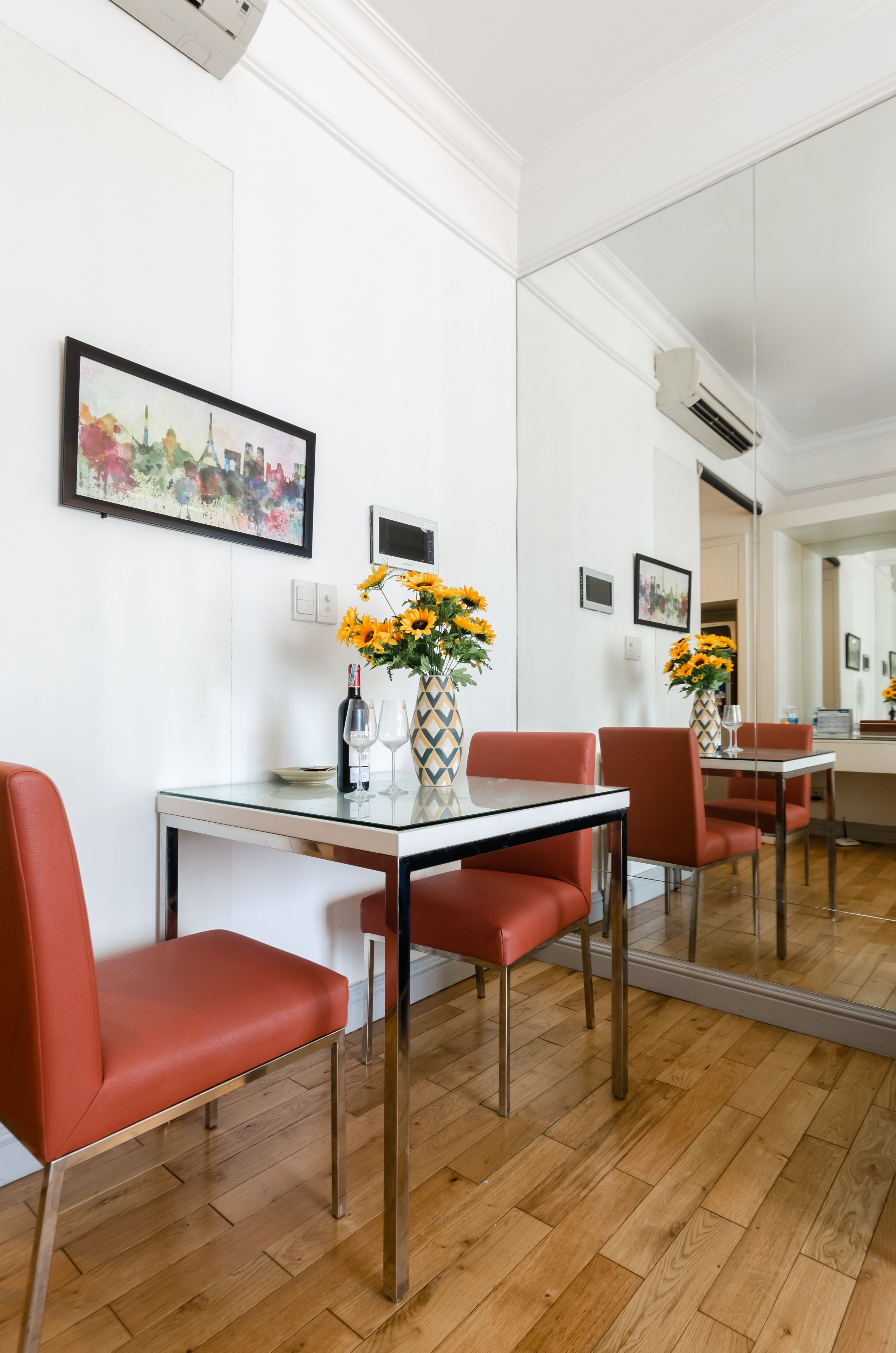 Un coin repas moderne avec une table en verre, des chaises rouges et un vase rempli de tournesols.