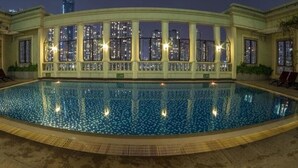 A large indoor swimming pool with a cityscape view, surrounded by columns and lounge chairs. - An Corner The Manor The Art - Saigon Central (Ho Chi Minh City)