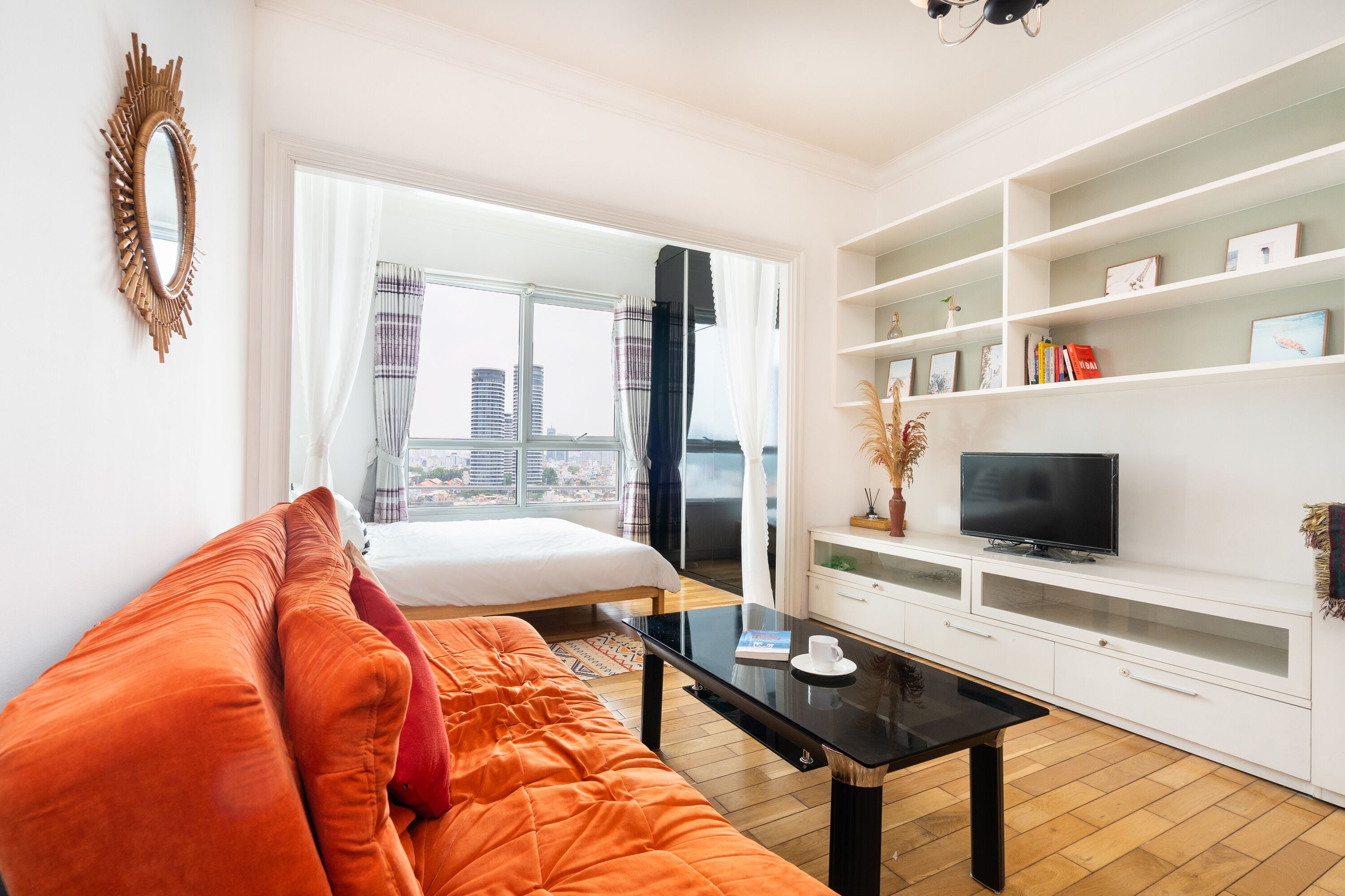 A modern living room with a sofa, a coffee table, a TV on a white cabinet, and a large window with curtains.