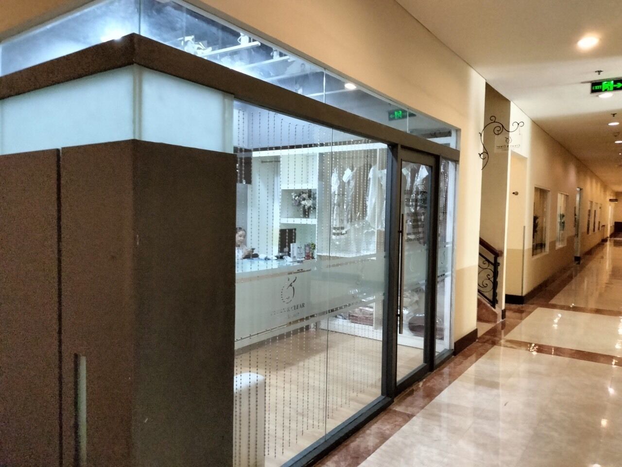 A corridor with a glass-fronted store, a staircase, and a sign indicating an exit.