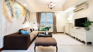A living room with a sofa, ottoman, and a TV on a white cabinet. - An Corner The Manor The Art - Saigon Central (Ho Chi Minh City)