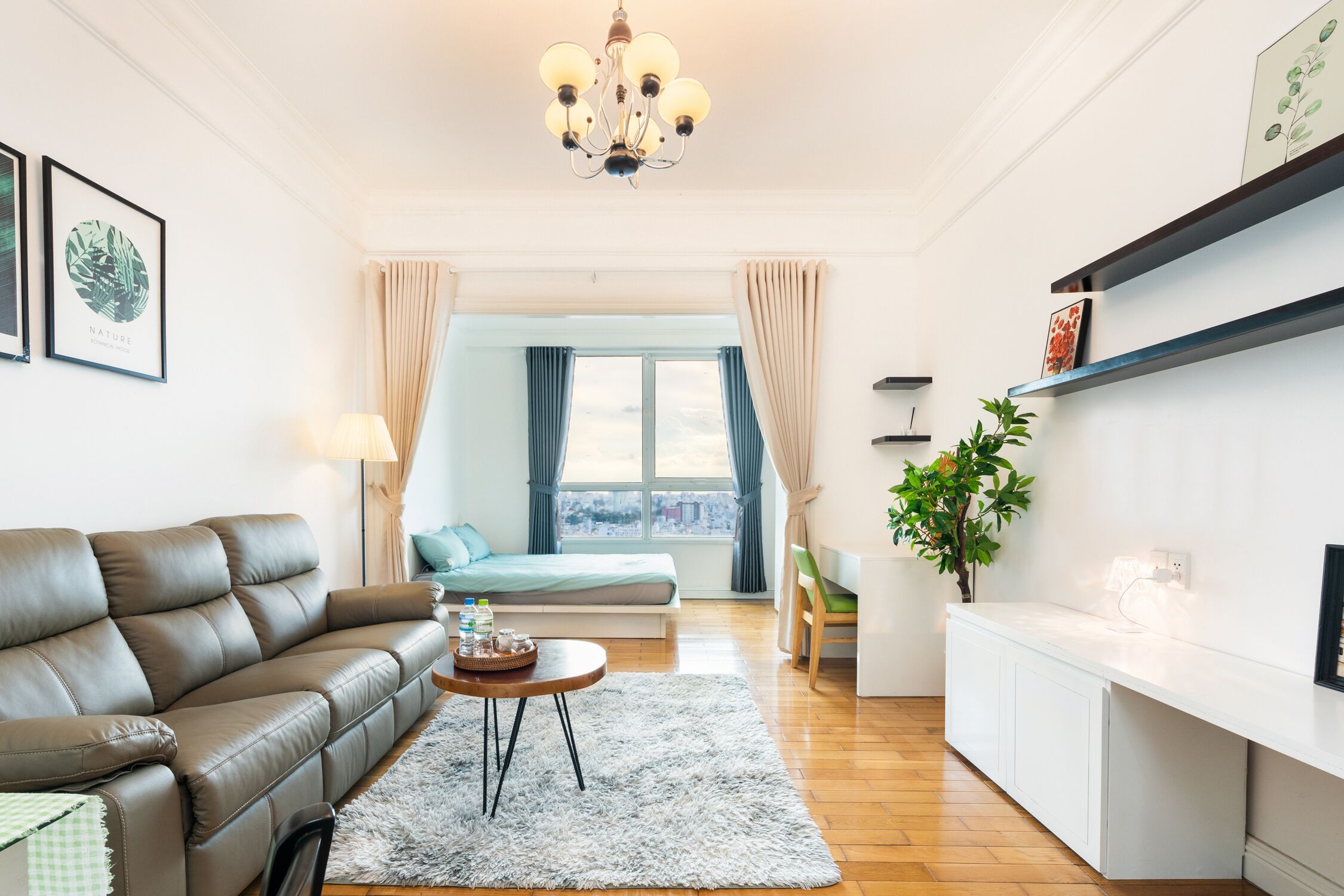 A modern living room with a leather sofa, a round coffee table, and a view of a cityscape through a large window.