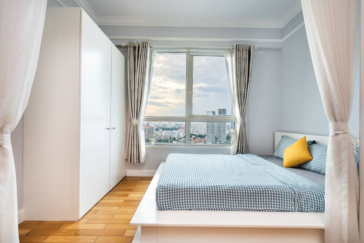 A bedroom with a city view, a bed with checkered bedding, and curtains.