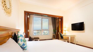 A hotel room with a large bed, a television mounted on the wall, a desk with a chair, and a window with a city view. - An Corner The Manor The Art - Saigon Central (Ho Chi Minh City)