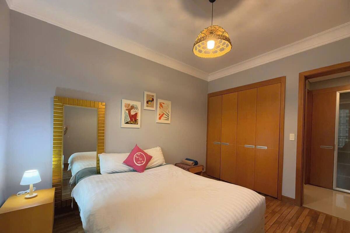 A bedroom with a large bed, a bedside table with a lamp, a wardrobe, and a mirror.