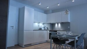 Una cocina moderna con armarios blancos, una mesa de comedor con sillas e iluminación colgante.