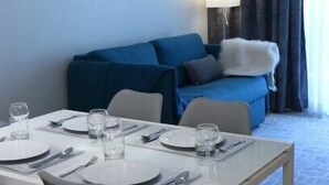 Un comedor con una mesa dispuesta para cuatro, un sofá azul y una lámpara al fondo.