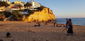 Une plage où l’on voit des gens se prélasser au soleil et se promener, une falaise avec des bâtiments, et la mer en arrière-plan.