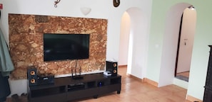 A living room with a stone wall, a flat-screen TV, a dark entertainment unit, and a door with an arched entrance.