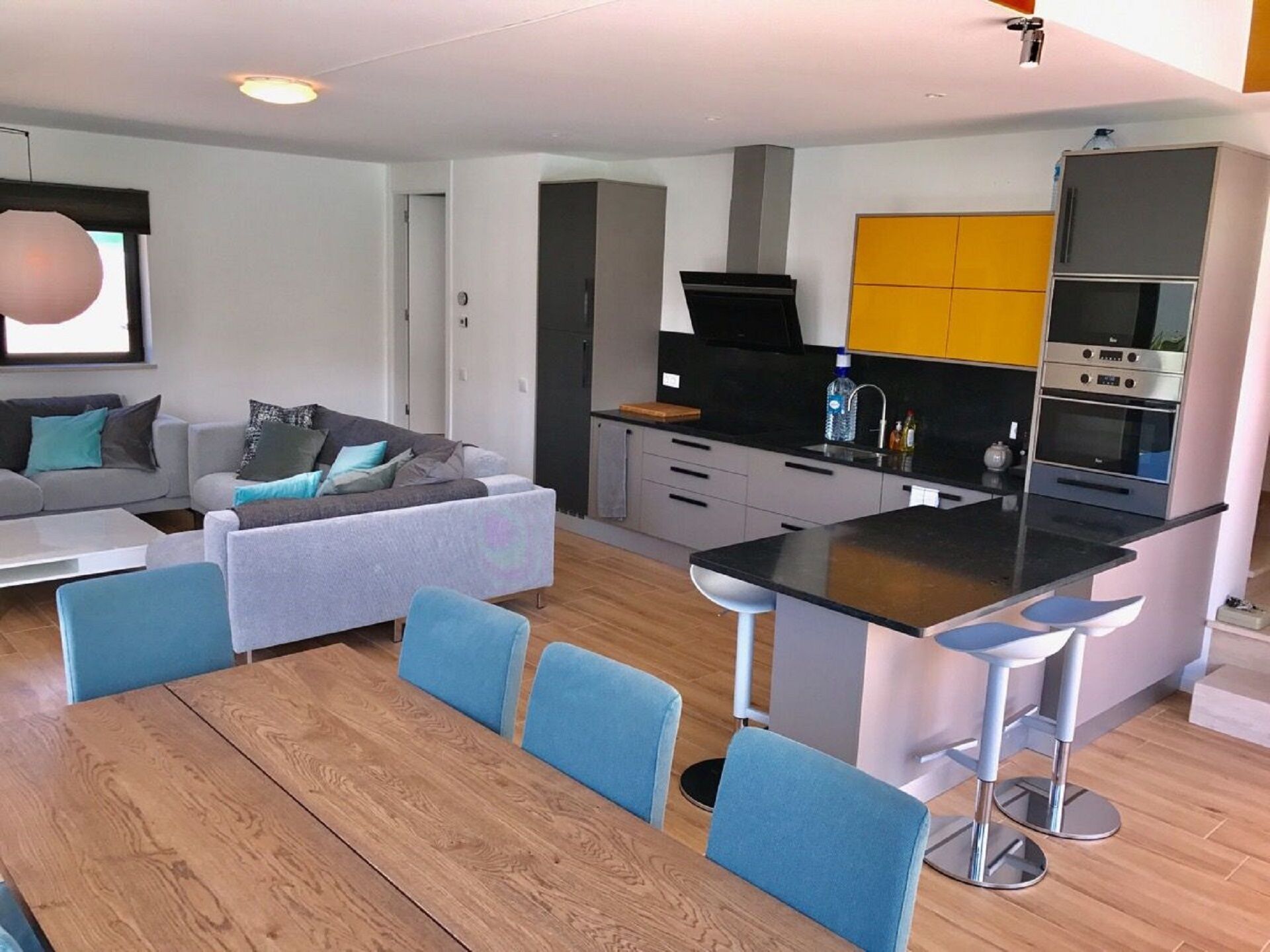 A modern kitchen with a central island, bar stools, and a dining table with chairs.