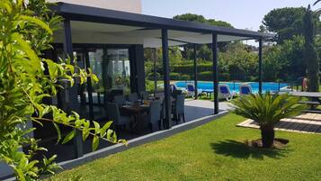 Un espace de restauration extérieur moderne, avec une piscine et des chaises longues en arrière-plan.