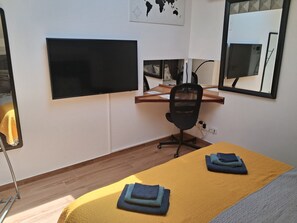 A hotel room with a bed, a desk, a chair, a flat-screen TV, and a large mirror.