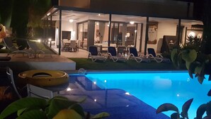 A modern hotel with a swimming pool, lounge chairs, and a well-lit interior. - Luxury detached villa with tropical garden and large private pool. Fully walled (Carvoeiro)