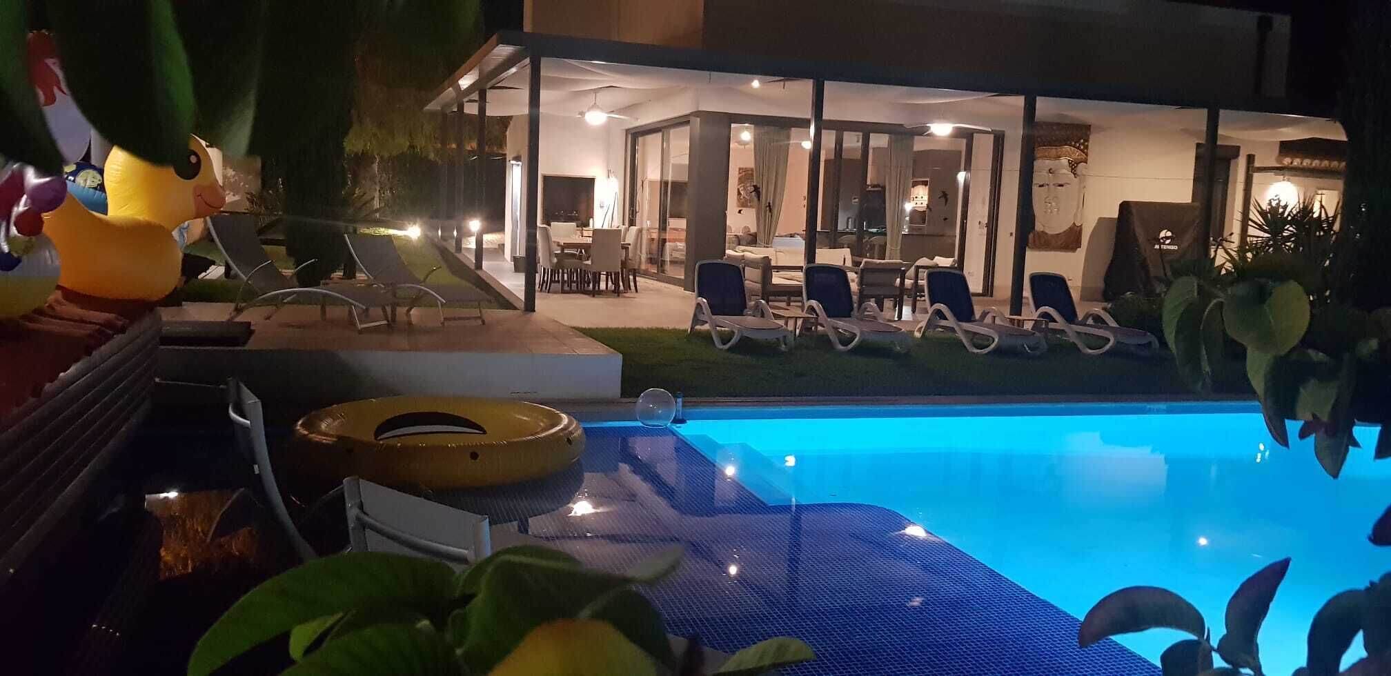 A swimming pool with lounge chairs, a glass-enclosed room with a dining area, and a statue.