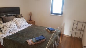 Een slaapkamer met een bed, kussens, een nachtkastje, een lamp, een raam en een metalen ladder.