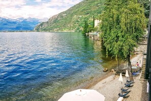 Udsigt over en sø med klart vand, en stenstrand og en række både.
