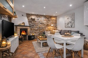 A cozy living room with a stone wall, a fireplace, a TV, and a dining area with chairs and a table.
