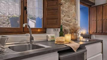Una cocina con un lavamanos de acero inoxidable, armarios de madera, una pared de piedra y una ventana con cortinas de encaje.