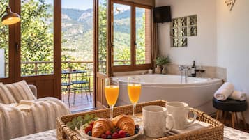 Desayuno con cruasanes, frutos rojos y jugo en una bandeja, una bañera y vistas a montañas a través de amplios ventanales.
