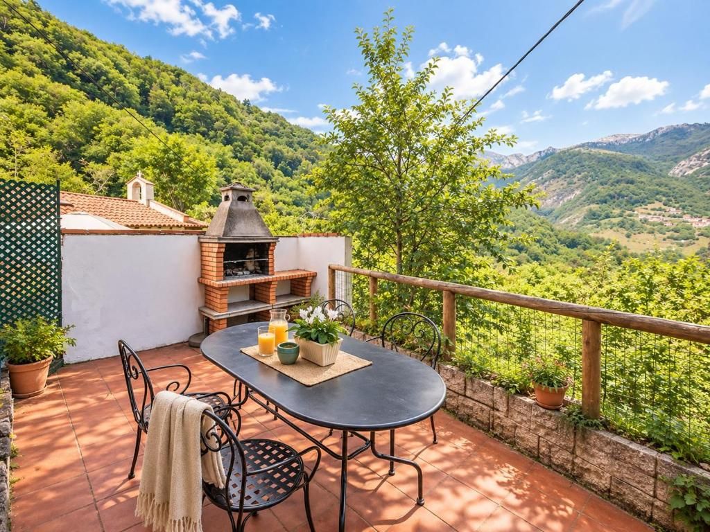 Un patio al aire libre con una mesa, sillas, un horno de ladrillo y vistas a un paisaje montañoso.
