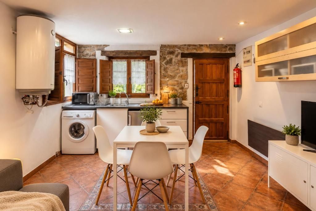 Cocina compacta con lavadora, microondas y comedor con sillas y mesa.