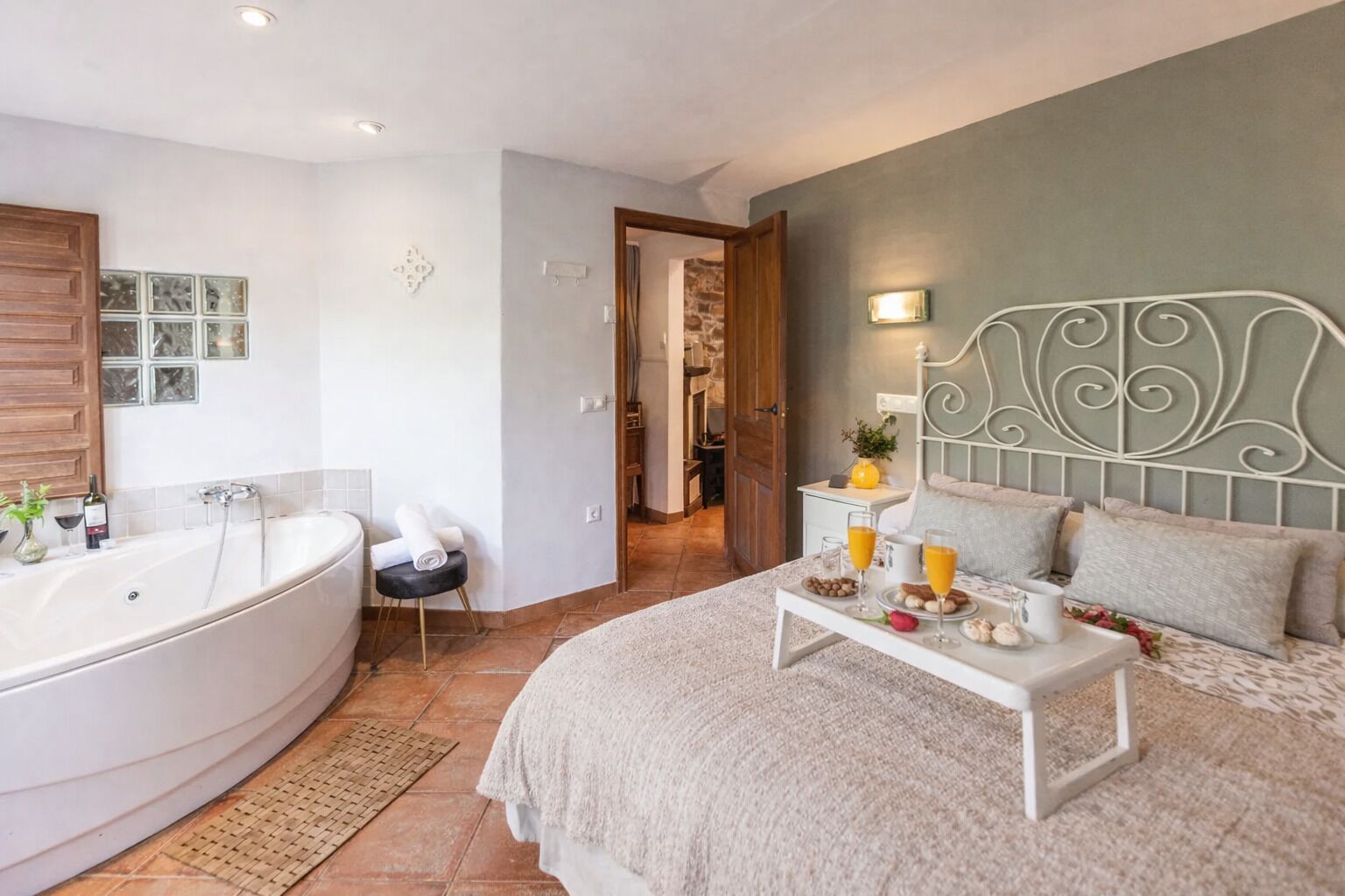 Un dormitorio con una cama grande, una mesita de noche con productos de desayuno, un baño con bañera y vistas a la cocina.