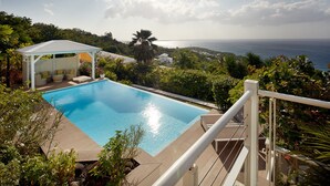 A swimming pool with a pergola and outdoor seating, surrounded by lush greenery and overlooking a coastal view. - Villa l'Amazonia 5 *, luxury villa rental in Deshaies in Guadeloupe: (Deshaies)