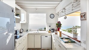 A modern kitchen with white cabinets, a dishwasher, a sink, and a window overlooking a scenic view. - Villa l'Amazonia 5 *, luxury villa rental in Deshaies in Guadeloupe: (Deshaies)