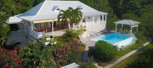 Une grande maison dotée d’une piscine, d’un patio couvert et d’un jardin luxuriant.