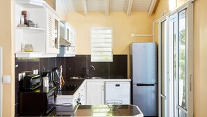 Une cuisine compacte équipée d’un réfrigérateur, d’un évier et d’un petit lave-vaisselle. Une fenêtre avec des stores laisse entrer la lumière, et la cuisine présente un design moderne avec des meubles blancs.