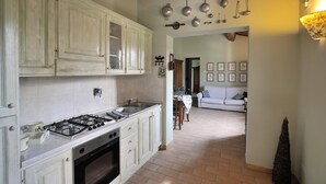 A kitchen with white cabinets, a gas stove, and a dining area with a table and chairs. - Apartment OLIVE TREE (Agriturismo Il Corniolo) (CORCIANO)