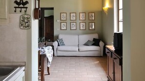 A kitchen with hanging pots and pans, a wooden ceiling, a sofa, and framed pictures on the wall. - Apartment OLIVE TREE (Agriturismo Il Corniolo) (CORCIANO)