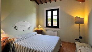 A bedroom with a bed, a window, a radiator, a lamp, and a wall decoration. - Apartment OLIVE TREE (Agriturismo Il Corniolo) (CORCIANO)