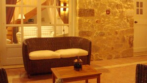 Une pièce chaleureuse avec un mur en pierre, un canapé en osier agrémenté de coussins, une table basse en bois et un meuble blanc.