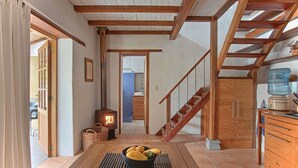 Ein gemütliches Interieur mit einer Holztreppe, einem zentralen Tisch mit Obst und einem Kaminofen.