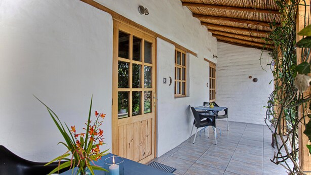 Eine überdachte Terrasse mit Tisch und Stühlen, eine Holztür und ein Fenster.