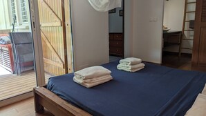 A bedroom with a bed, a wooden bench, a wooden door, and a view of the outside. - Maison Forban - Villa Ti-Polo (Deshaies)