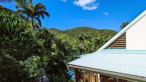 A house with a corrugated metal roof, surrounded by lush greenery and a mountainous backdrop. - Maison Forban - Villa Ti-Polo (Deshaies)