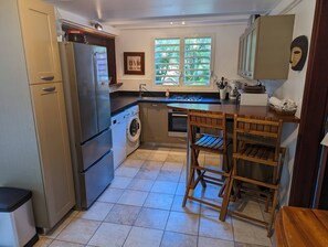 A compact kitchen with a built-in washing machine, a stove, and a sink. - Maison Forban - Villa Ti-Polo (Deshaies)