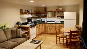 Una cocina compacta con armarios de madera, un microondas y un lavabo. Hay una mesa de comedor con sillas y un sofá en la sala de estar.