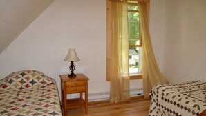 Un dormitorio con dos camas, una mesita de noche con lámpara, una ventana con cortinas y piso de madera.