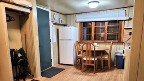 Une cuisine de taille réduite, équipée d’un réfrigérateur, de chaises en bois, d’une table à manger et d’une fenêtre avec des stores.