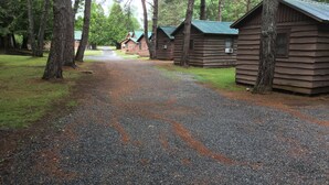 Un sentier de gravier mène à des chalets en bois dotés de toits verts, qui sont eux-mêmes entourés d’arbres.