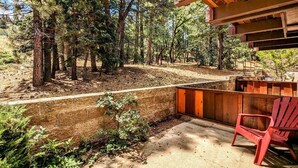 A covered outdoor area with a concrete floor, surrounded by trees and a wooden deck.