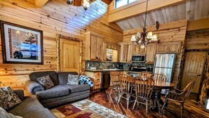 A cozy cabin interior with a wooden interior, a sofa, a dining table with chairs, and a kitchen area.